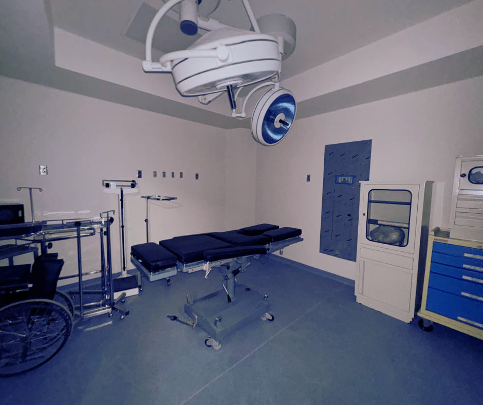 Un quirófano con cama quirúrgica, equipo médico y lámparas de techo. Predominan los tonos azules y blancos.