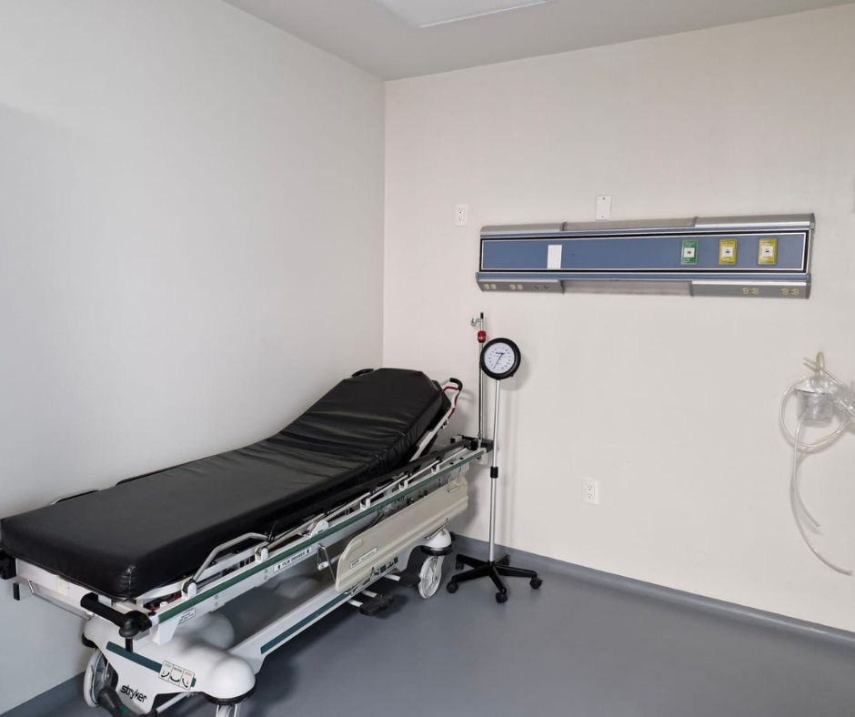 Habitación de hospital vacía con una camilla, equipo médico montado en la pared y un suelo.