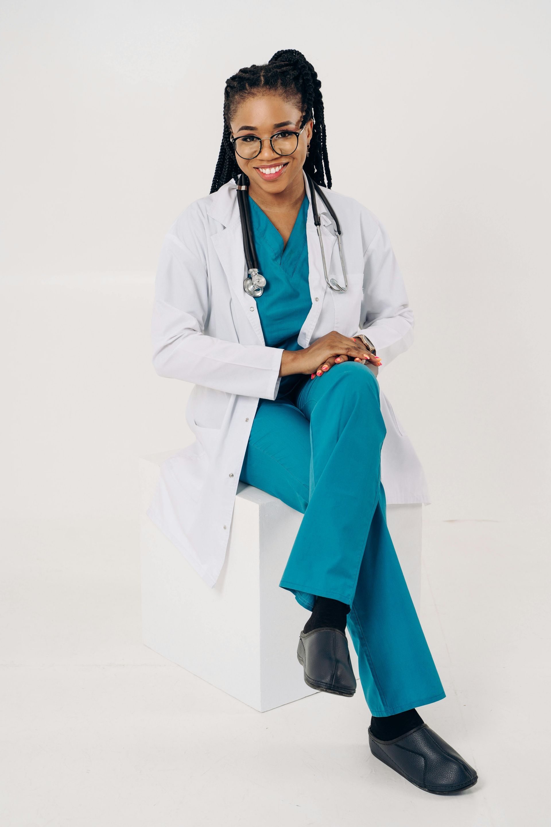 Profesional médico con uniforme y bata de laboratorio de color verde azulado, sentado con un estetoscopio, sonriendo.