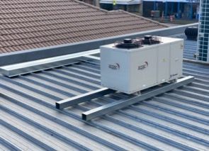 Hvac Unit On A Metal Beam Platform On A Corrugated Metal Roof — Refrigeration & Air Conditioning in Jewells, NSW