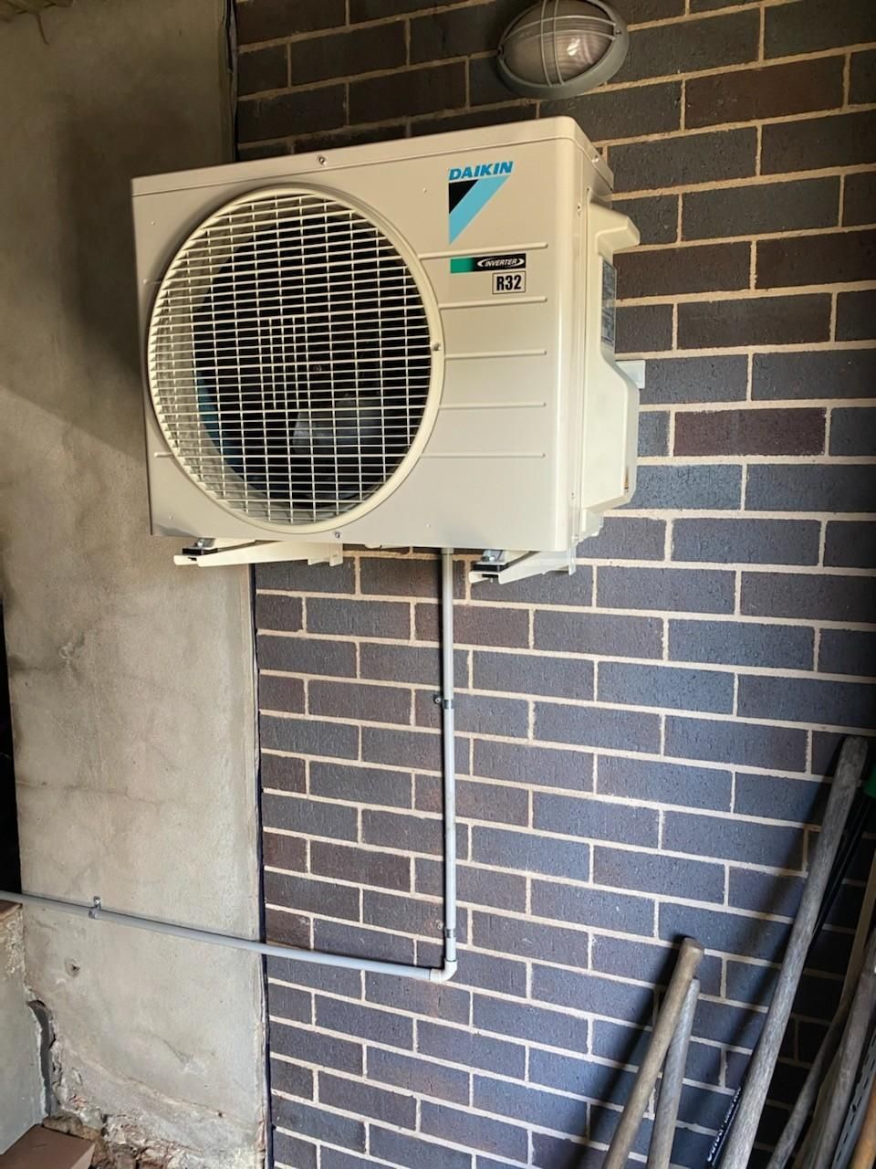 Daikin Air Conditioner Mounted on A Brick Wall with Conduit and An Outdoor Light Fixture — Refrigeration & Air Conditioning in Central Coast, NSW