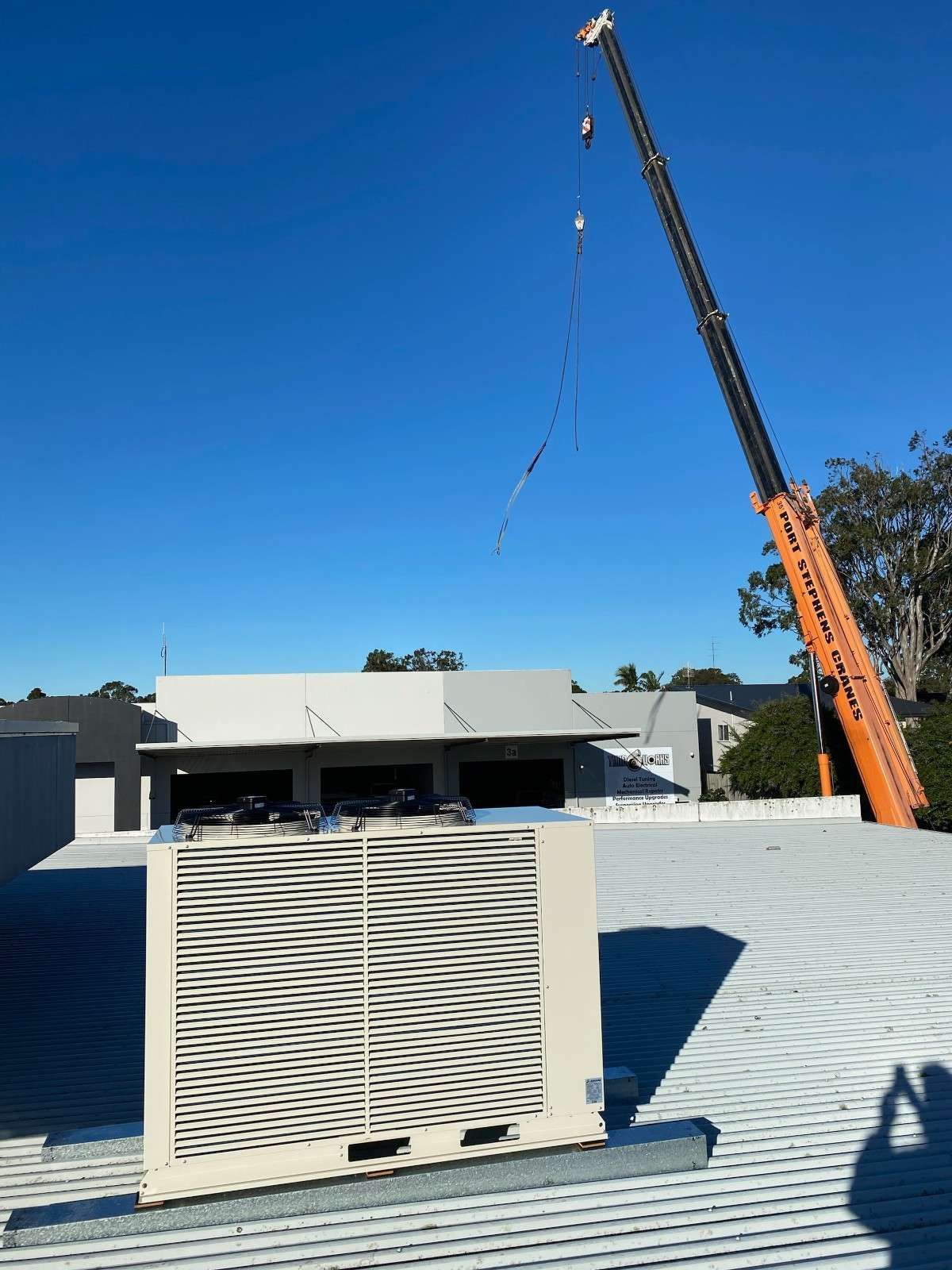 A Crane Lifting an Air Conditioning Unit onto A Rooftop on A Sunny Day — Refrigeration & Air Conditioning in Newcastle, NSW