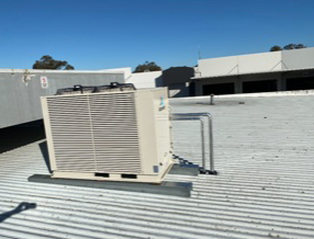 Hvac Unit On A Metal Roof Against A Clear Blue Sky — Refrigeration & Air Conditioning in Jewells, NSW
