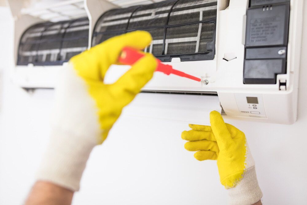 Person Uses Screwdriver to Service a White Air Conditioner — Refrigeration & Air Conditioning in Warners Bay, NSW