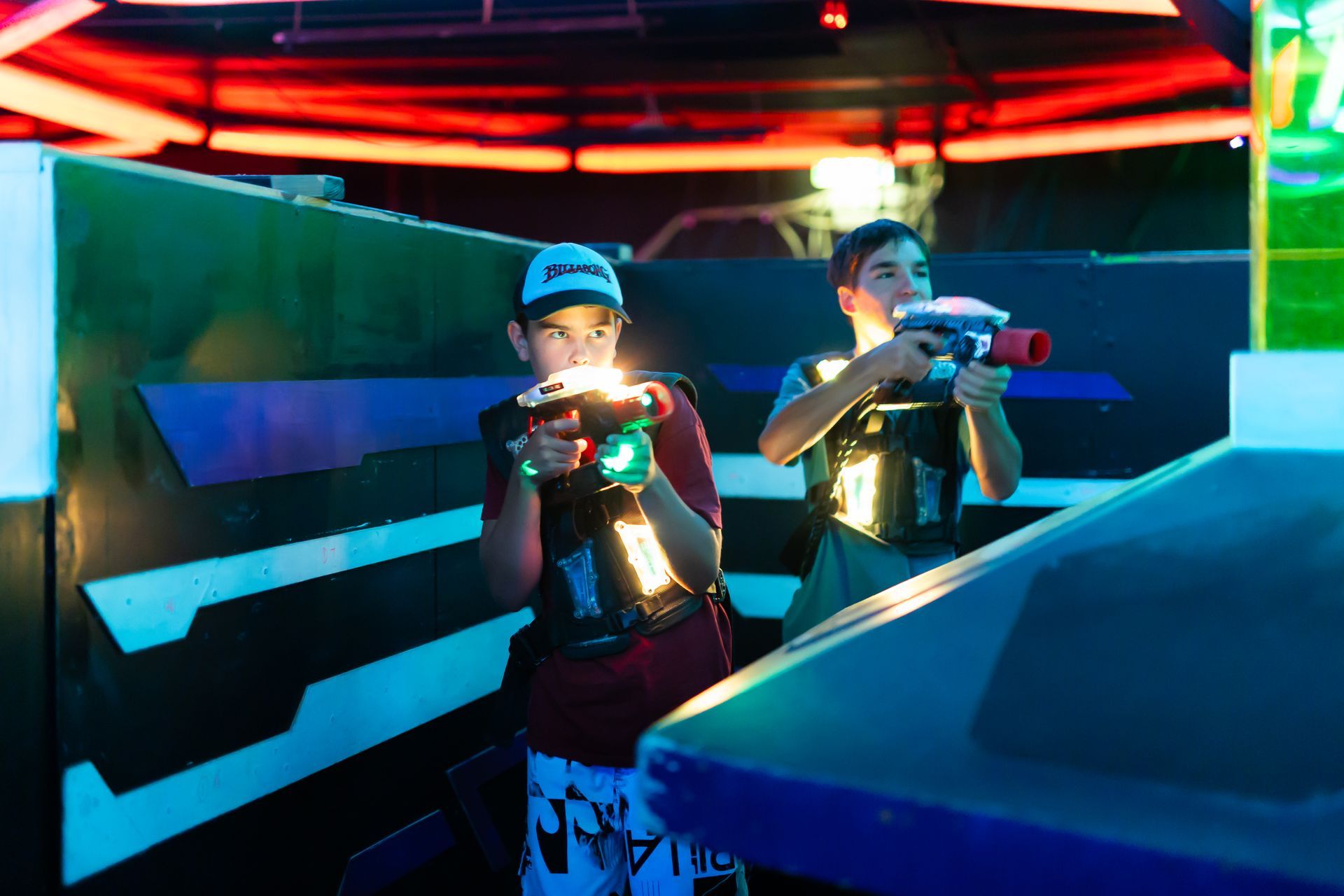 Two people at Laserzone Sunshine Coast playing laser tag, wearing vests, and illuminated with colored lights.