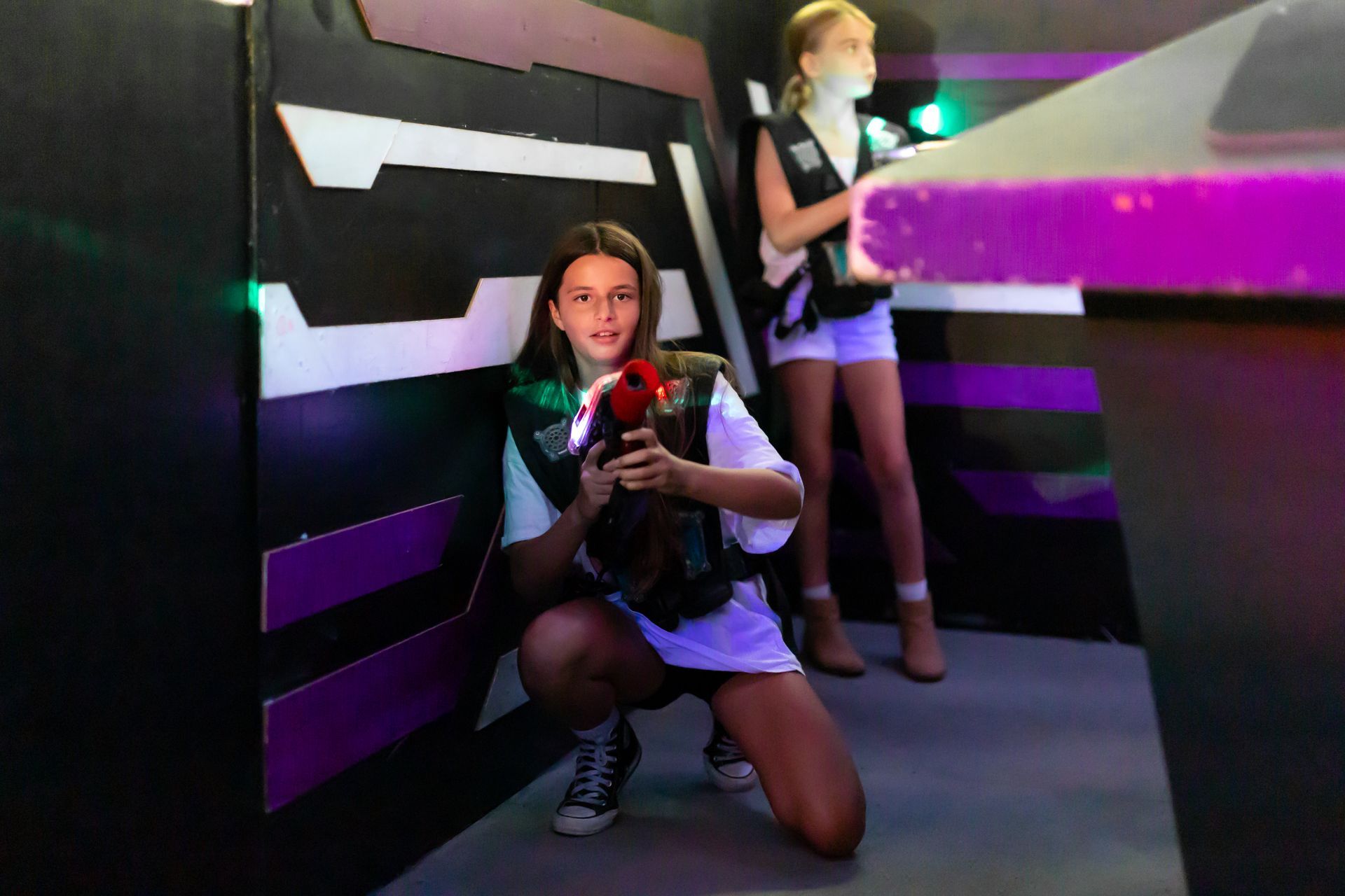 Two people playing laser tag in an arena at Laserzone Sunshine Coast. One is crouching with a phasor, another stands nearby.
