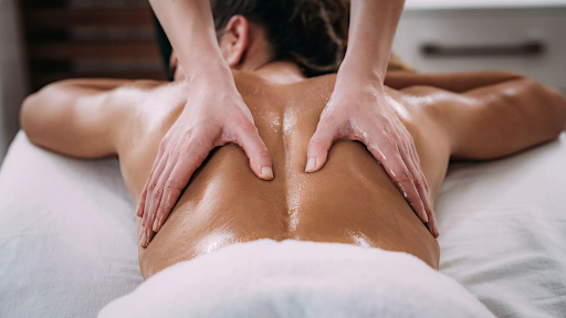 Pregnant person giving massage on stomach of another person on a massage table, light room.