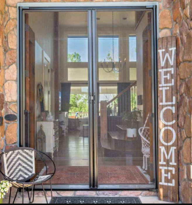 Double screen doors open to a home's interior, a welcome sign, and a chair.