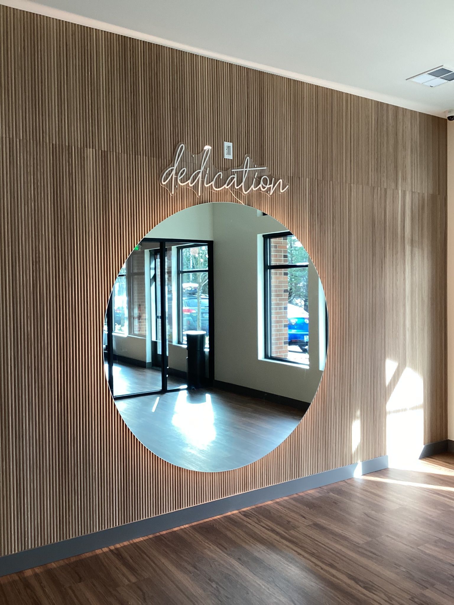 Acoustic wall paneling with a large round mirror reflecting a room with windows and a neon sign 