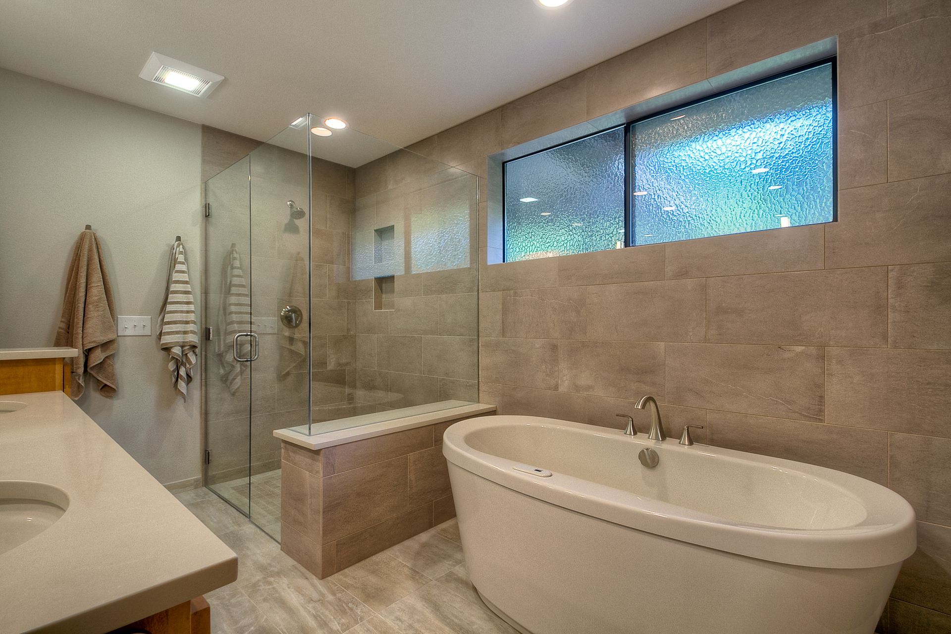 Modern bathroom with a freestanding tub, glass shower, and large window.