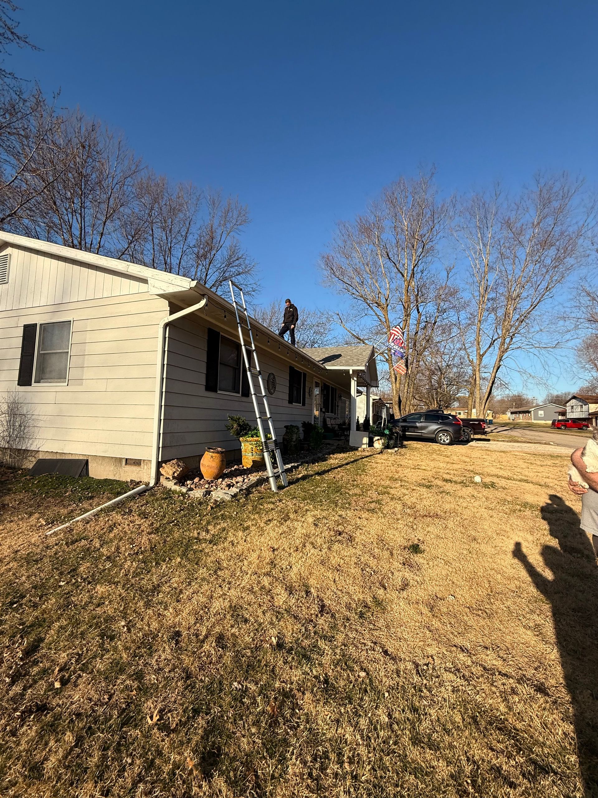 Person on a ladder, working on the roof of a house on a sunny day.