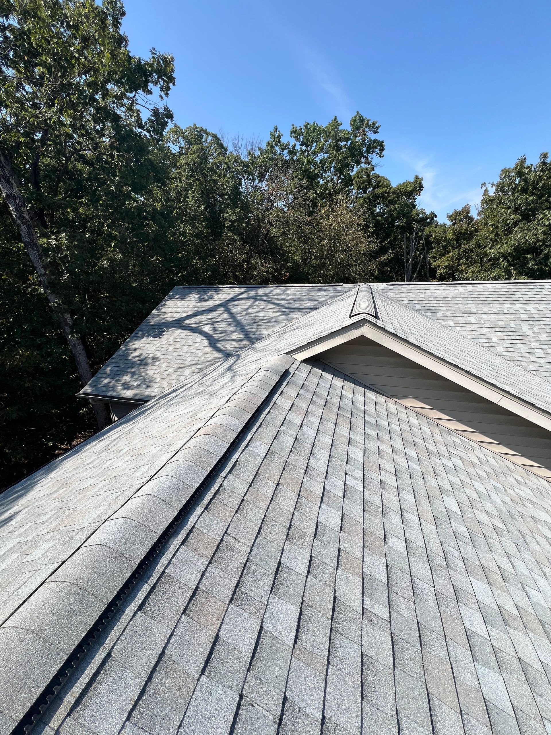 Black gutter system on a modern building's corner with wood-look siding. Blue sky and clouds above.