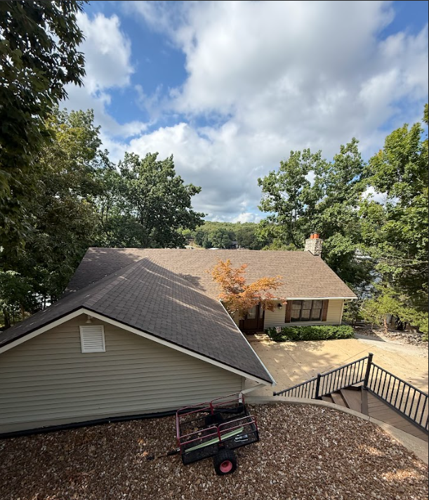 House with a brown roof surrounded by trees under a cloudy sky.