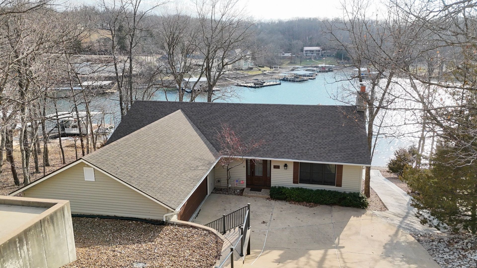 An elevated view of a light-colored house with a dark brown roof, situated next to a cove with docked boats.