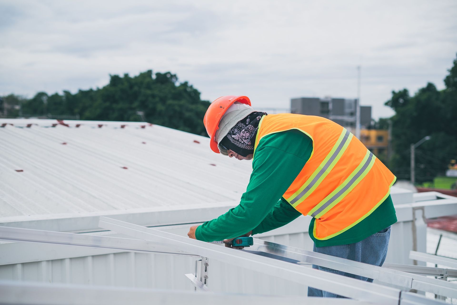 A construction worker wearing safety gear working on rooftop installation outdoors