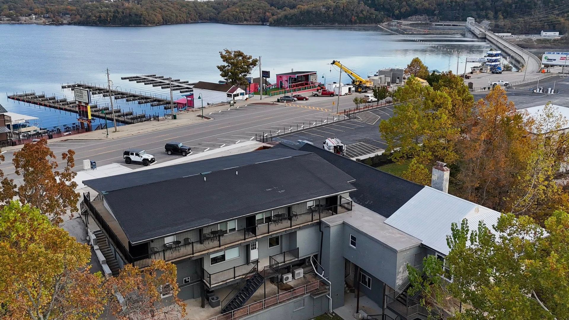 Aerial view of a gray building with black roof near a marina and lake with a bridge.