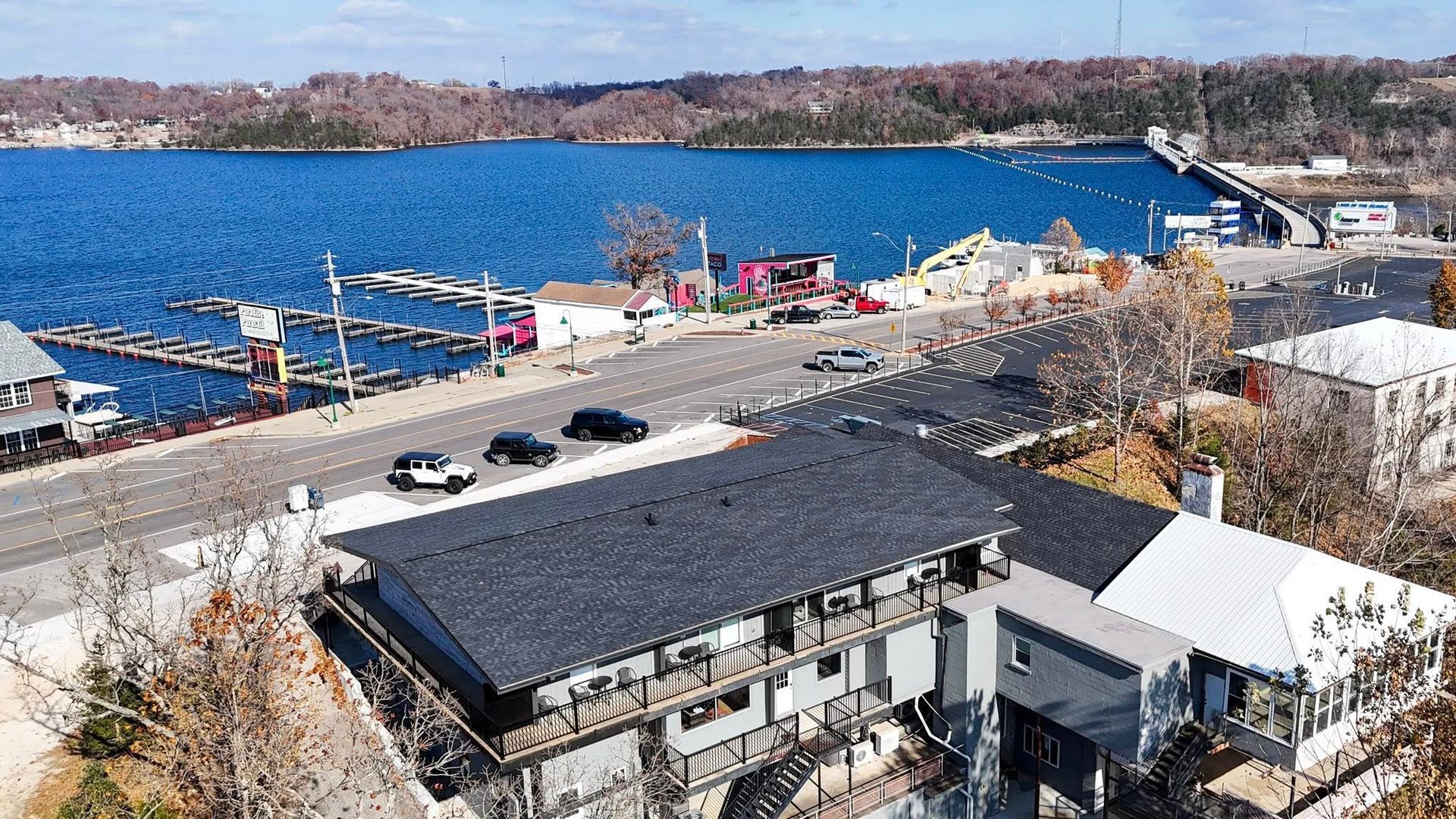 Overhead view of a lakefront street with a bridge in the distance; marina and buildings line the road.