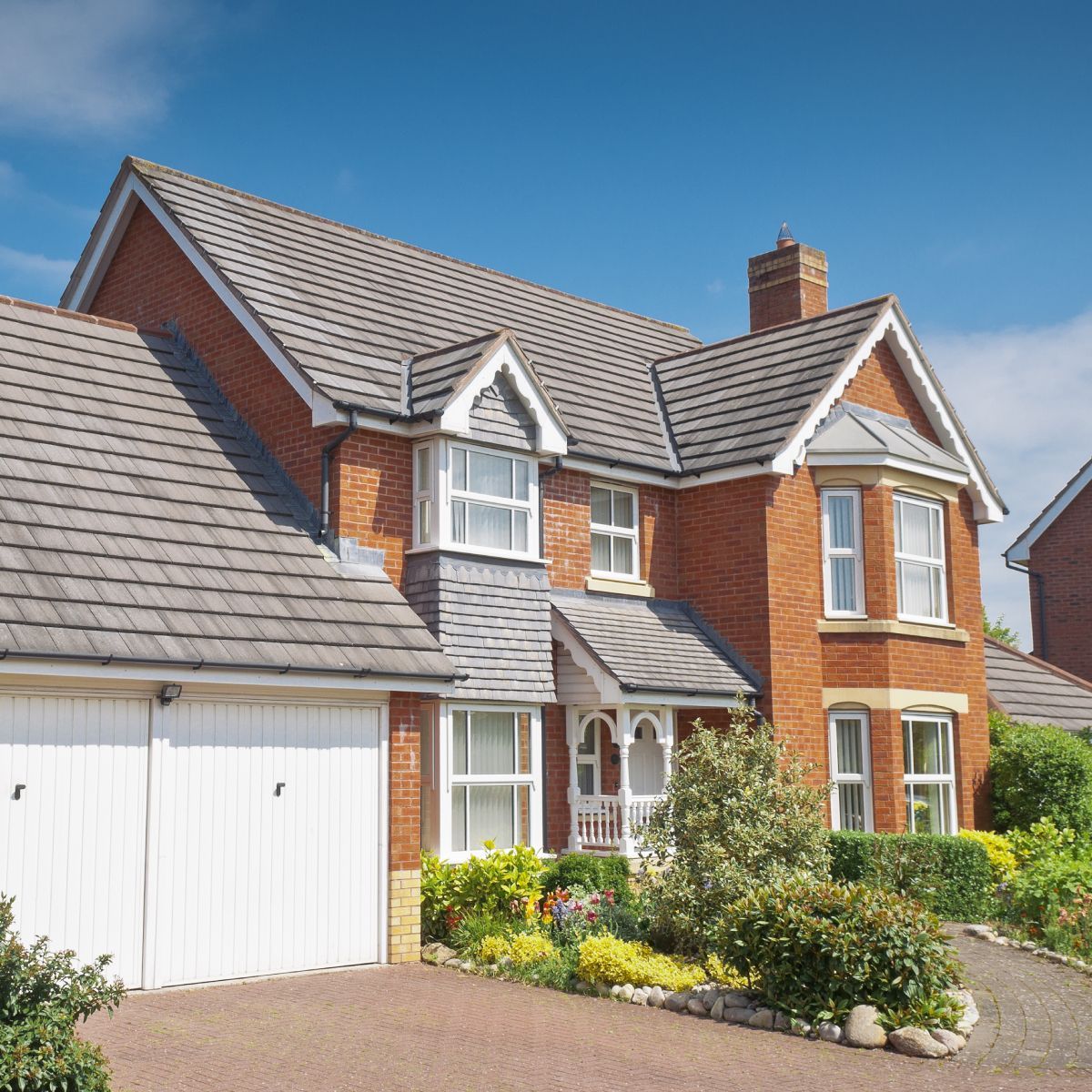 Red brick two-story house with white garage doors, gray roof, and blue sky.
