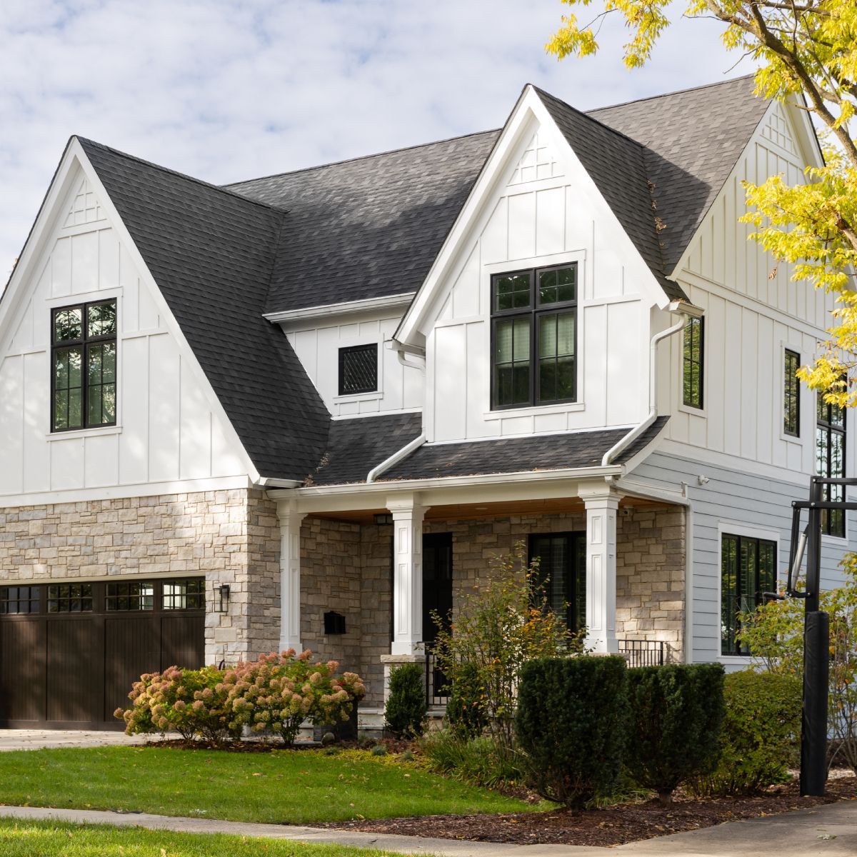 White house with gray stone accents, black windows, and dark roof, on a sunny day.