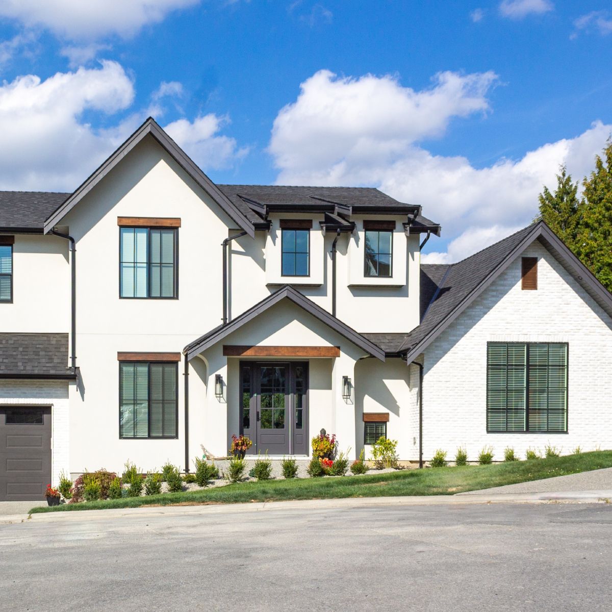 White two-story house with dark trim, gray roof, and a sunny blue sky.