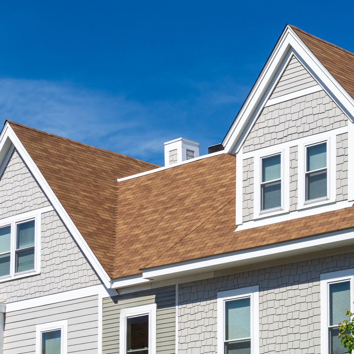 Gray house with brown roof against a blue sky.