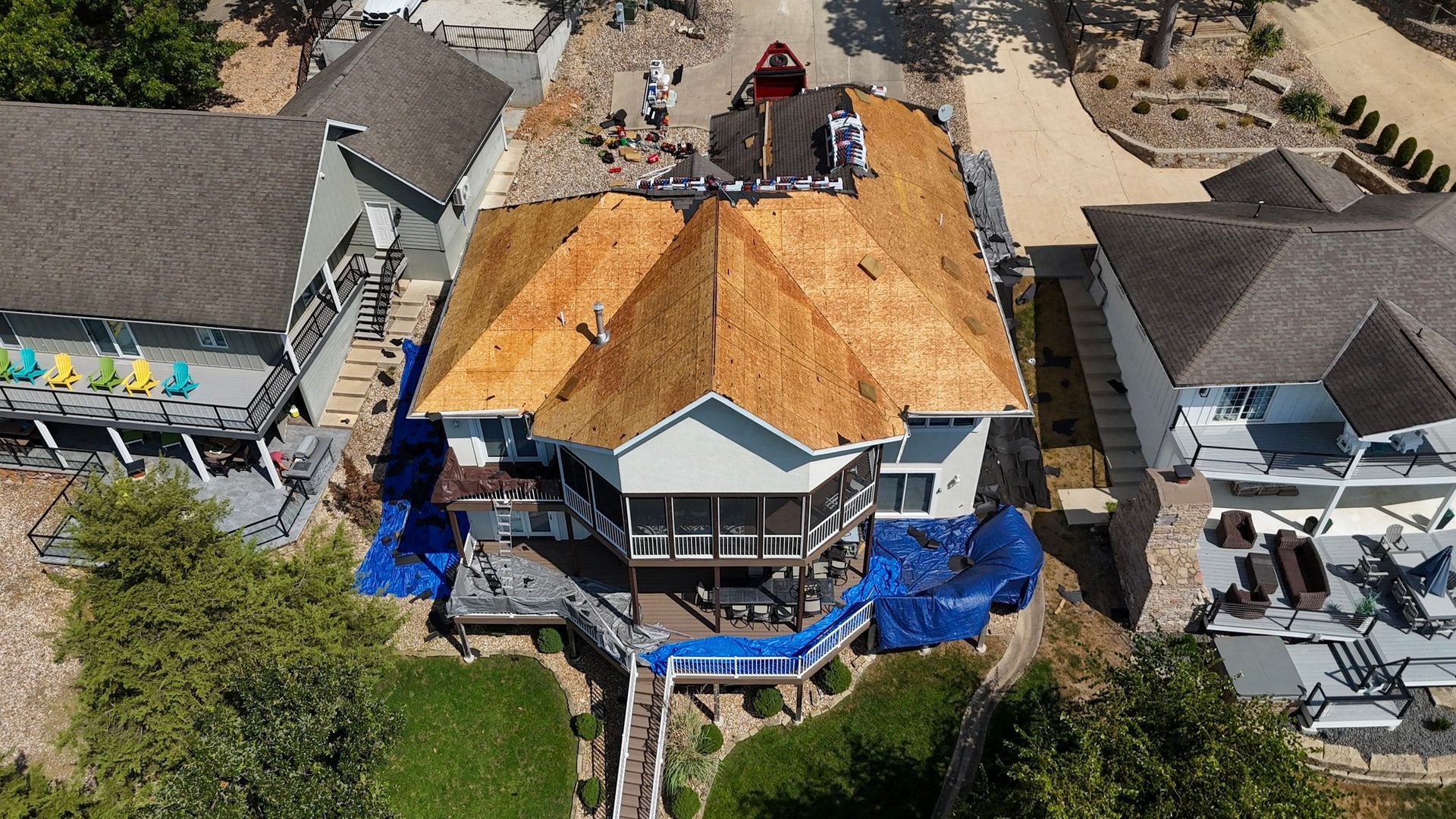 Aerial view of a house undergoing roof replacement with blue tarps protecting the lower areas.
