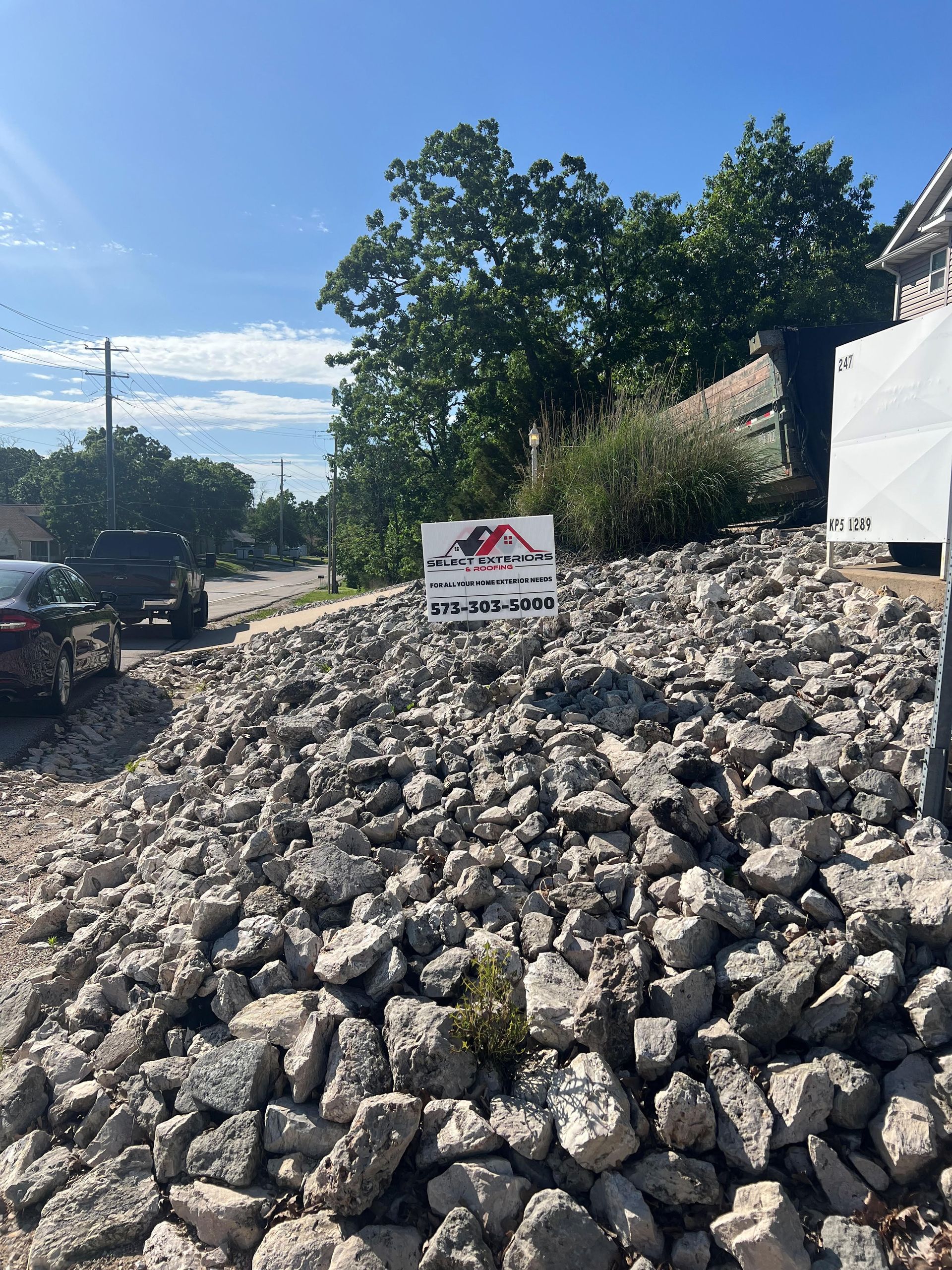 Construction site with large pile of rubble, sign in front of a house.