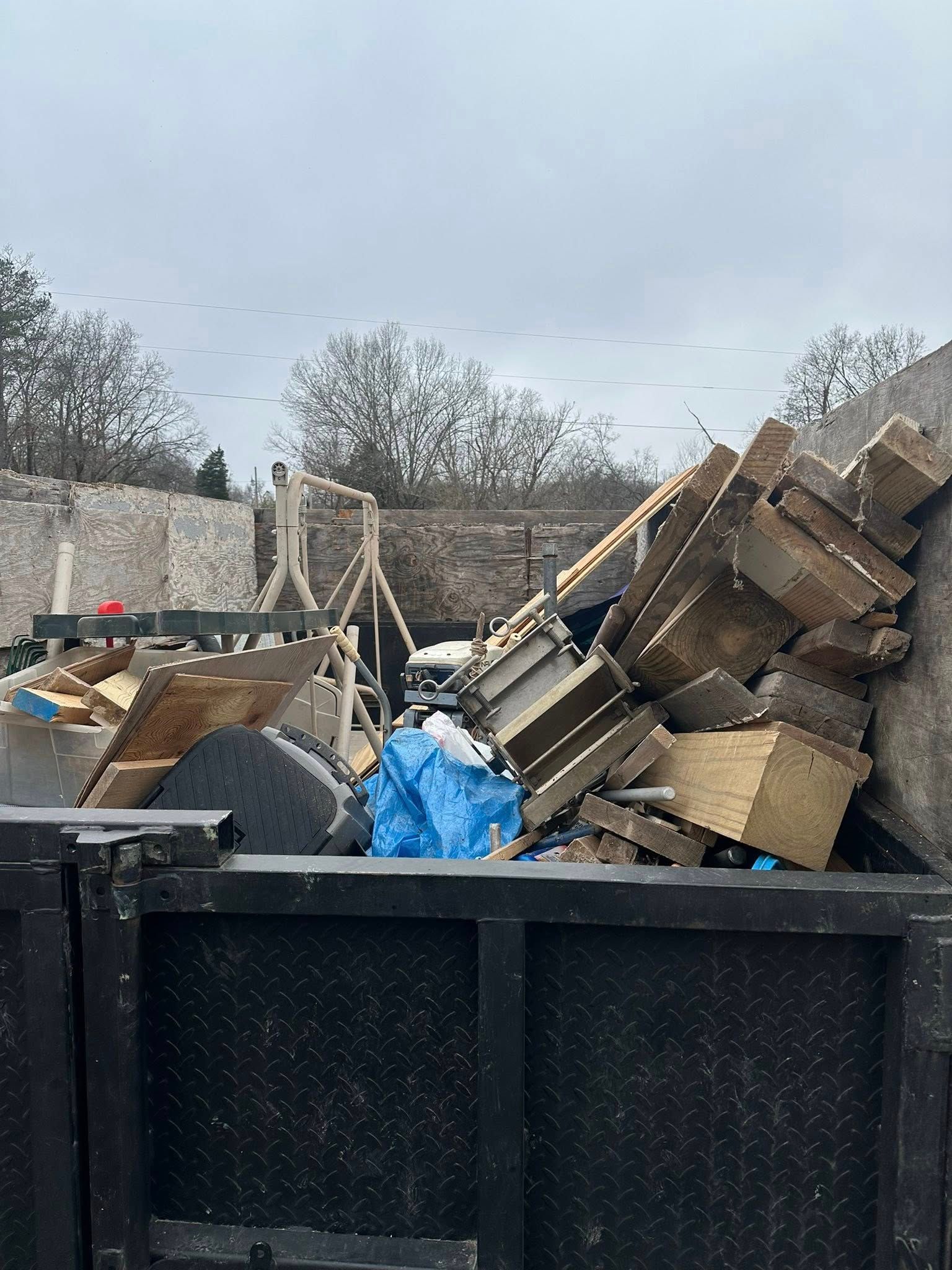 Dumpster filled with mixed debris and broken wood in an outdoor construction or cleanup area