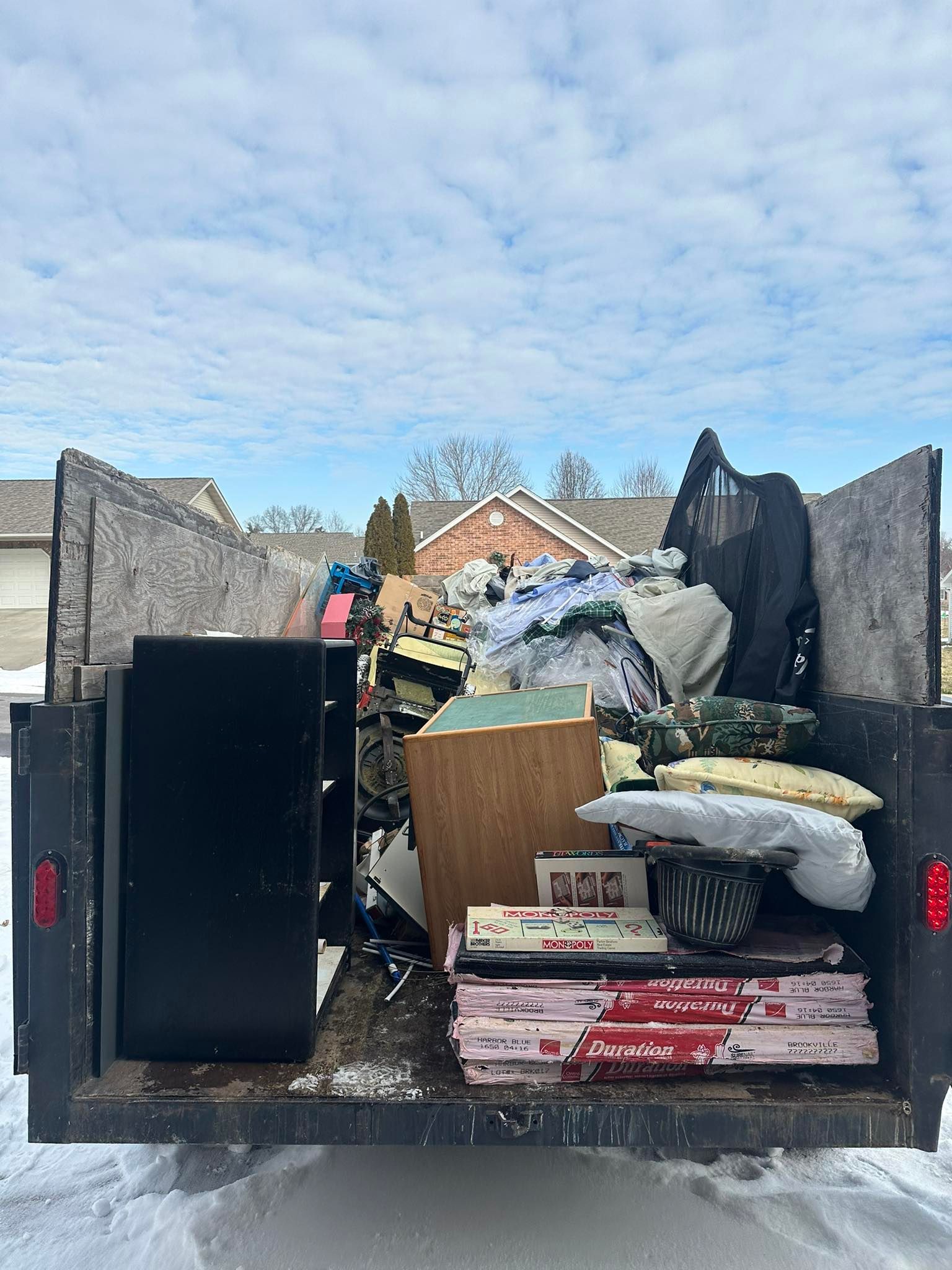 Open dumpster overflowing with trash and discarded furniture outside houses under a cloudy sky