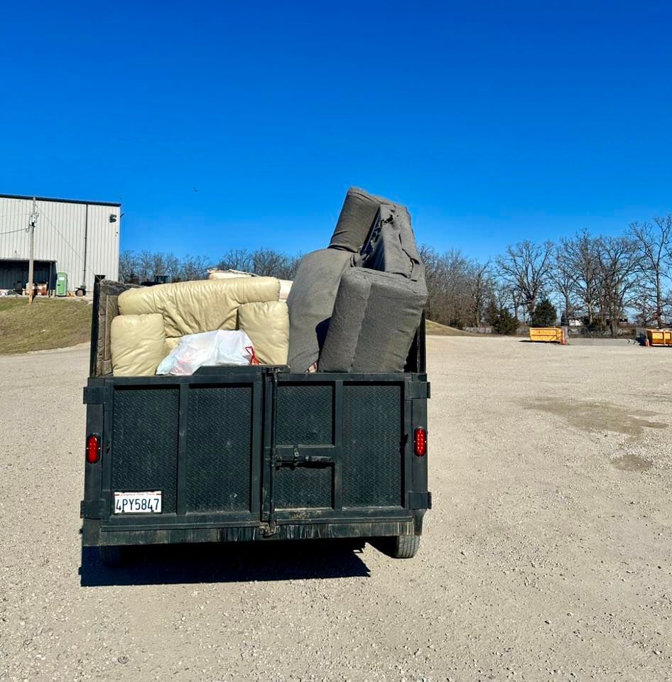 Loaded trailer hauling large wrapped bundles on a gravel lot under a clear blue sky