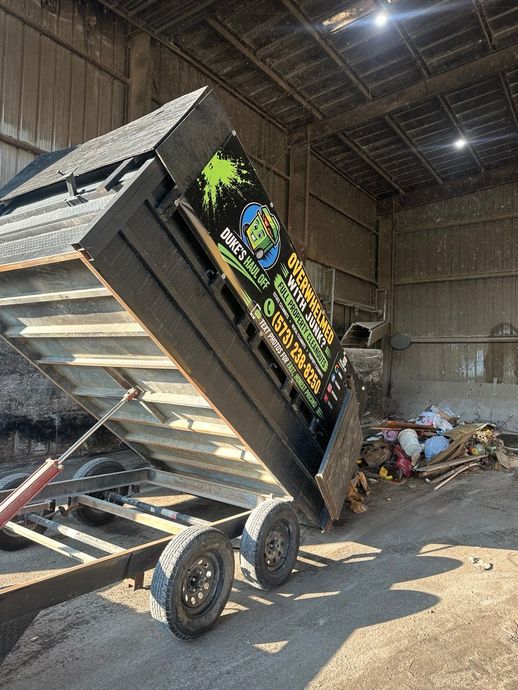 Red pickup truck bed piled high with cardboard and household debris outdoors under a blue sky