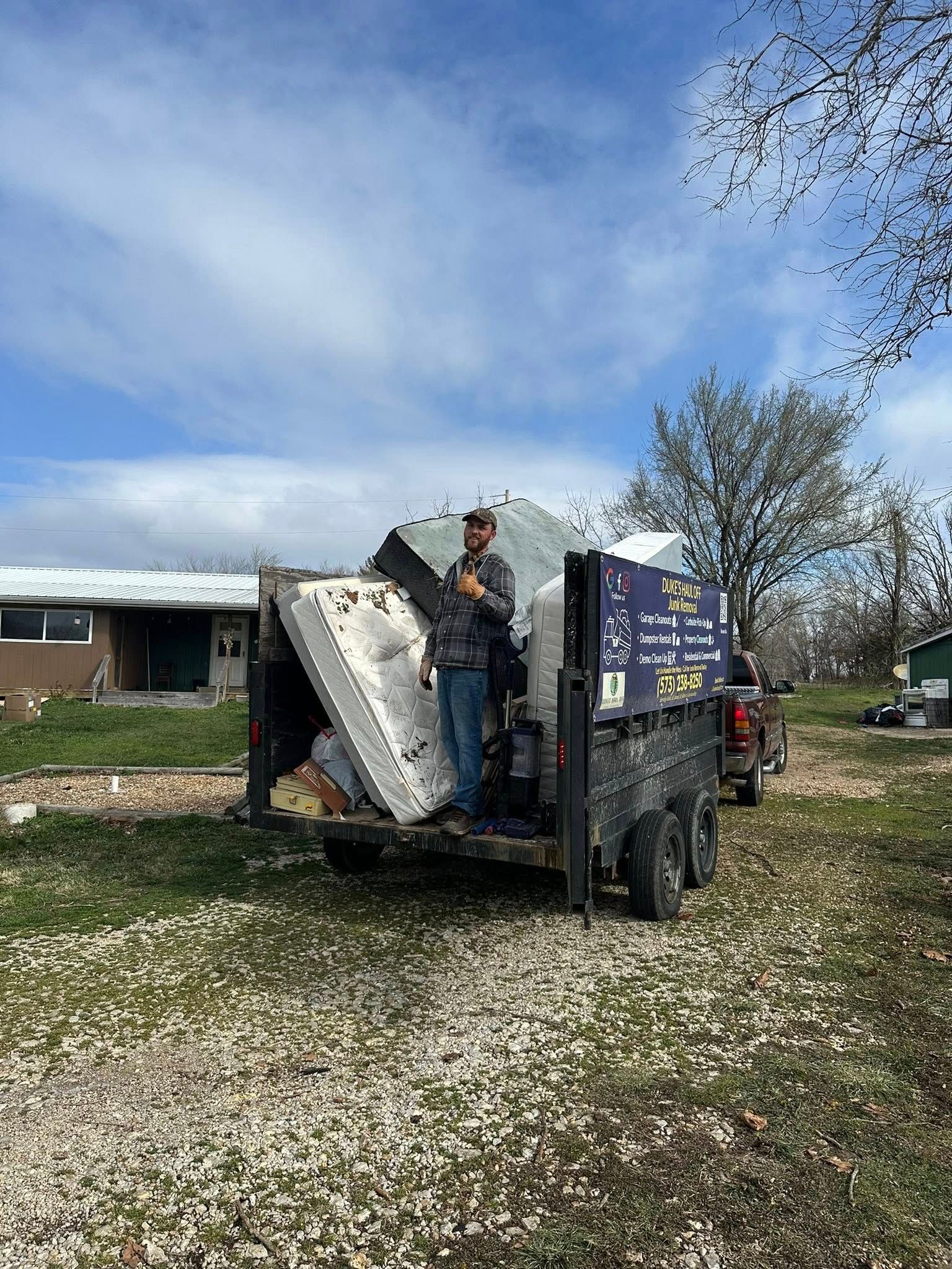 Worker on a truck dumping debris in a yard under a blue sky