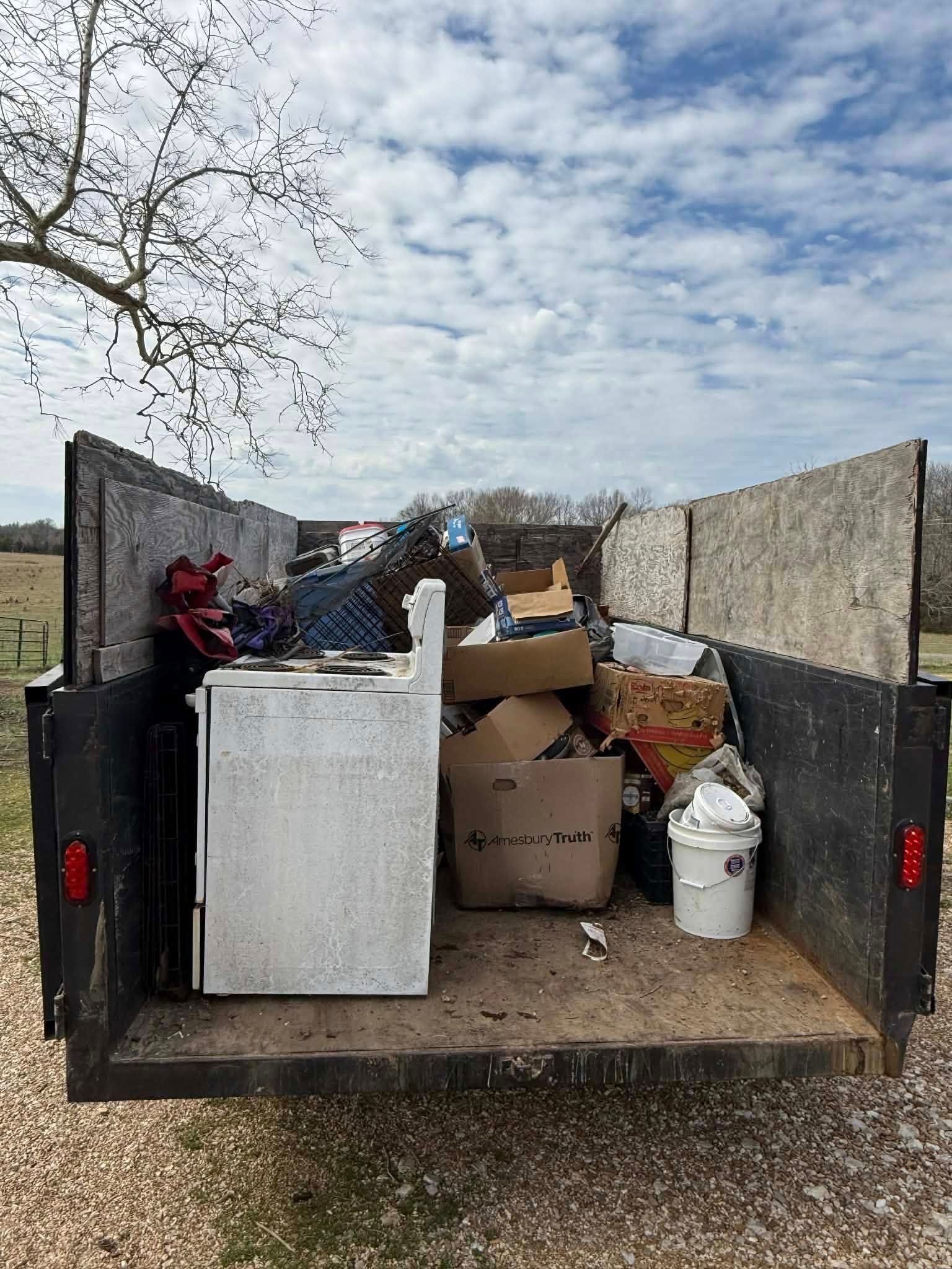Pickup truck bed filled with boxes, a white appliance, and assorted household items outdoors