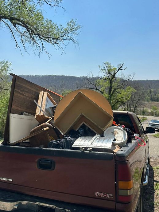 Red pickup truck bed piled high with cardboard and household debris outdoors under a blue sky