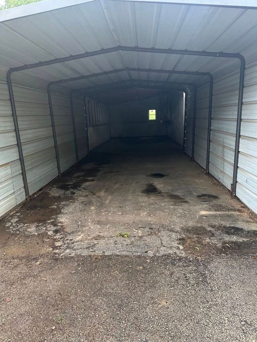 Empty metal garage with gravel floor, dark interior, and a small bright opening at the far end