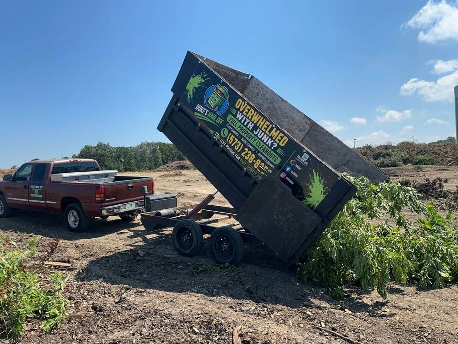 Pickup towing a trailer with a large blue sign along a muddy roadside under cloudy skies