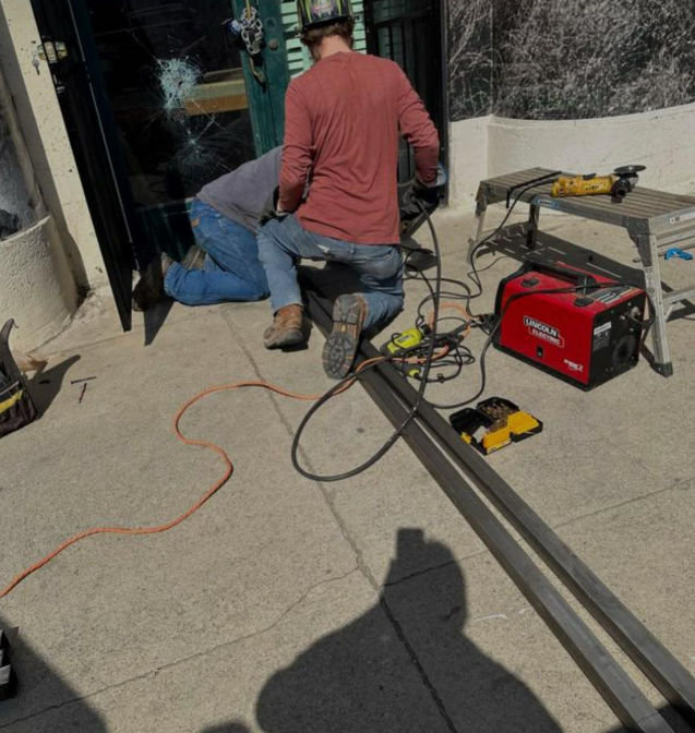 Worker kneeling by a building entrance beside tools and a red generator on a concrete patio