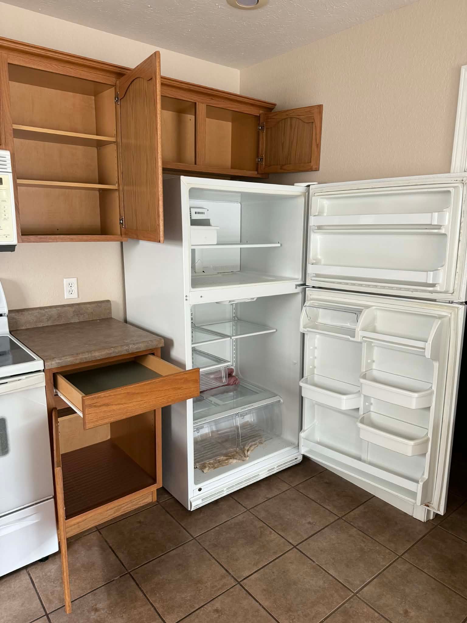 Open kitchen with white refrigerator, open wooden cabinets, and a small rolling cart on tiled floor