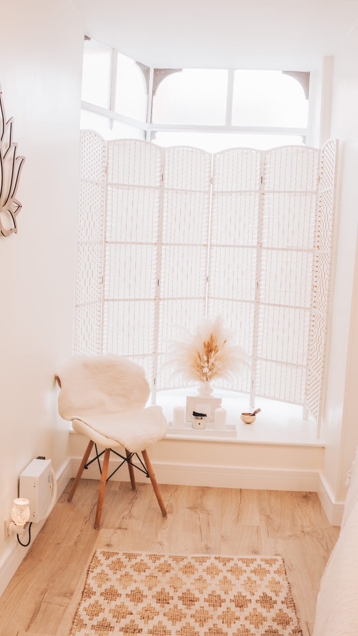 Cozy window nook with a white chair, macrame screen, and a rug. Dried flowers and decor on the windowsill.