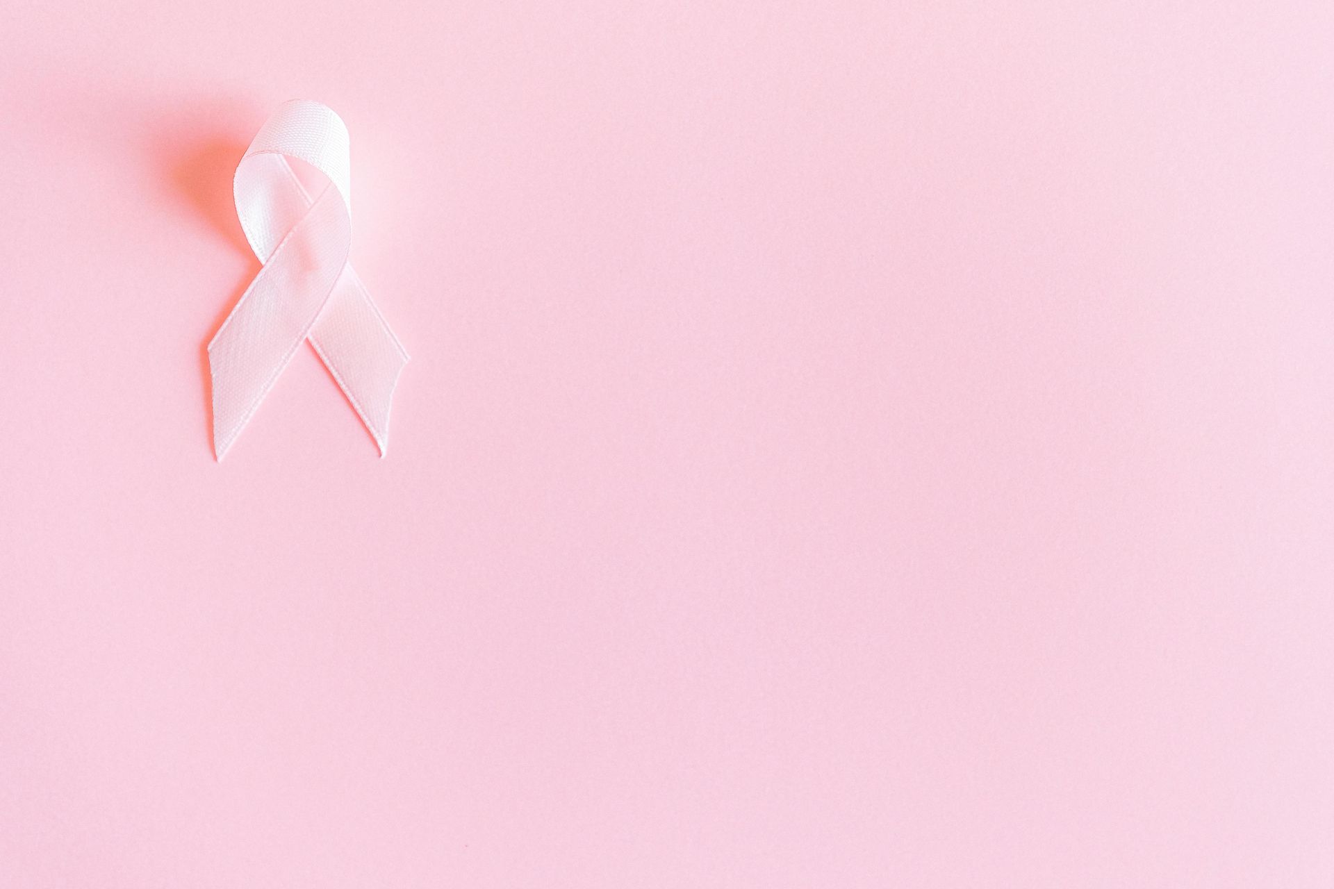 A white breast cancer awareness ribbon on a pink background.