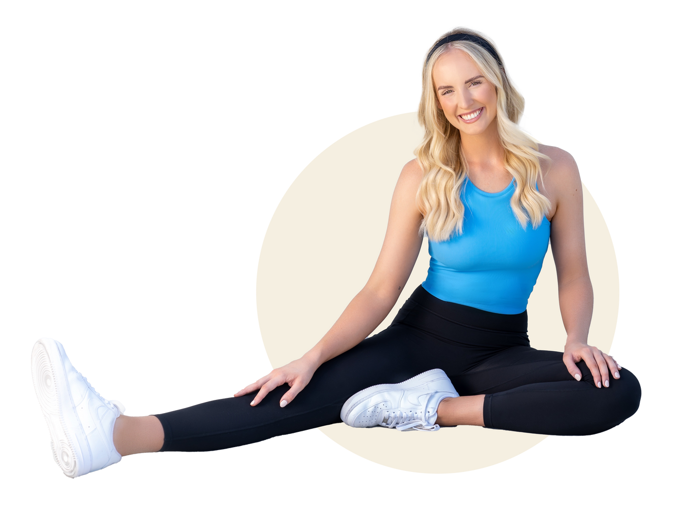 A woman in a blue tank top and black leggings is sitting on the floor with her legs crossed.