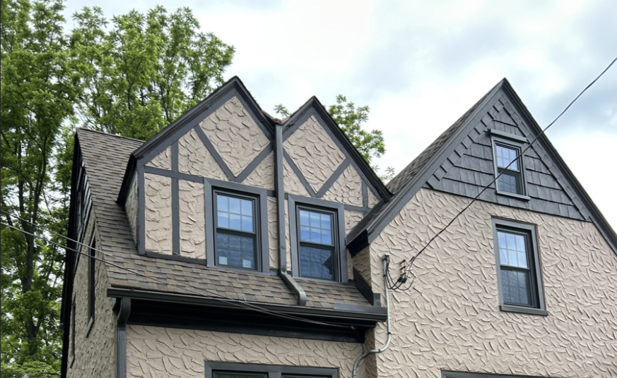 Two-story Tudor-style house exterior with beige brick, dark trim, and gabled roofline