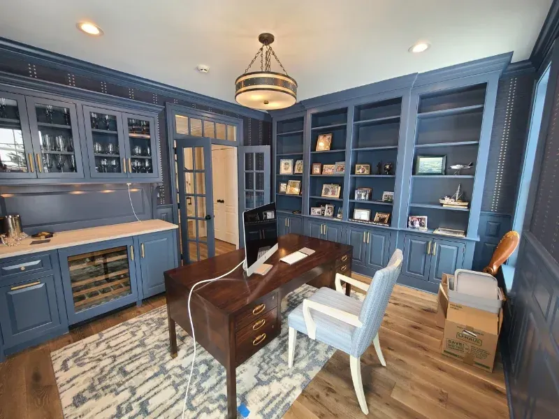 A home office with a desk , chairs , shelves and a wine cooler.