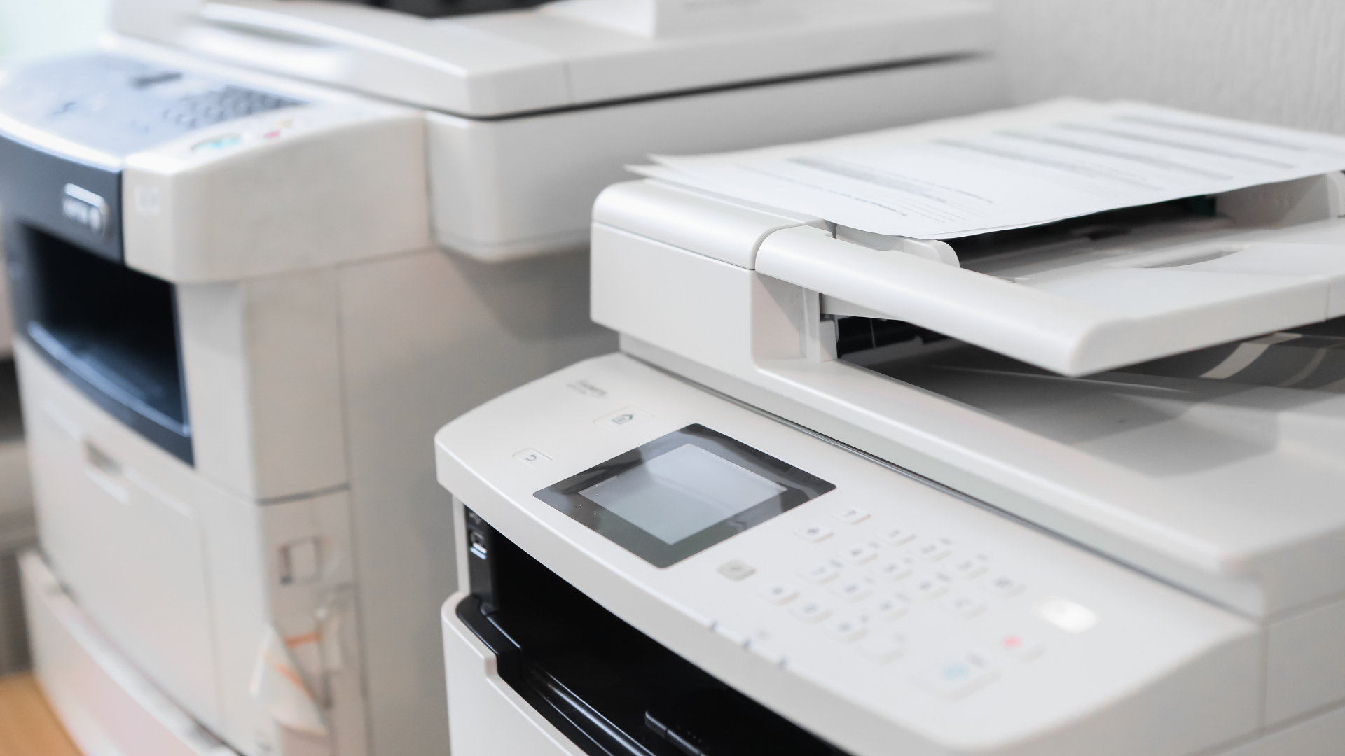 Two copiers/printers are sitting next to each other in a room
