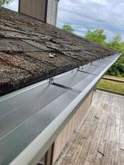Damaged roof edge with missing shingles and loose silver gutter above a wooden deck