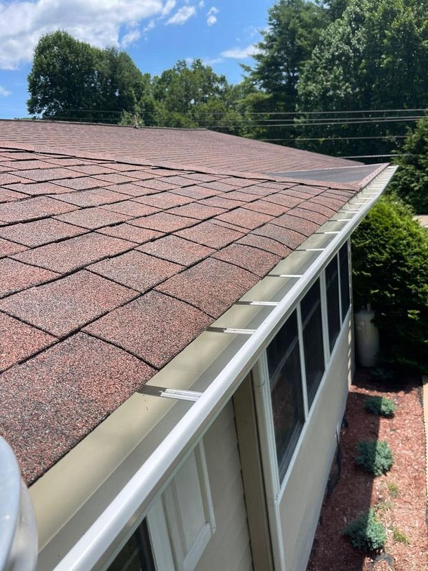 Brown shingle roof with gutters and white trim on a house, viewed from above amid trees and blue sky