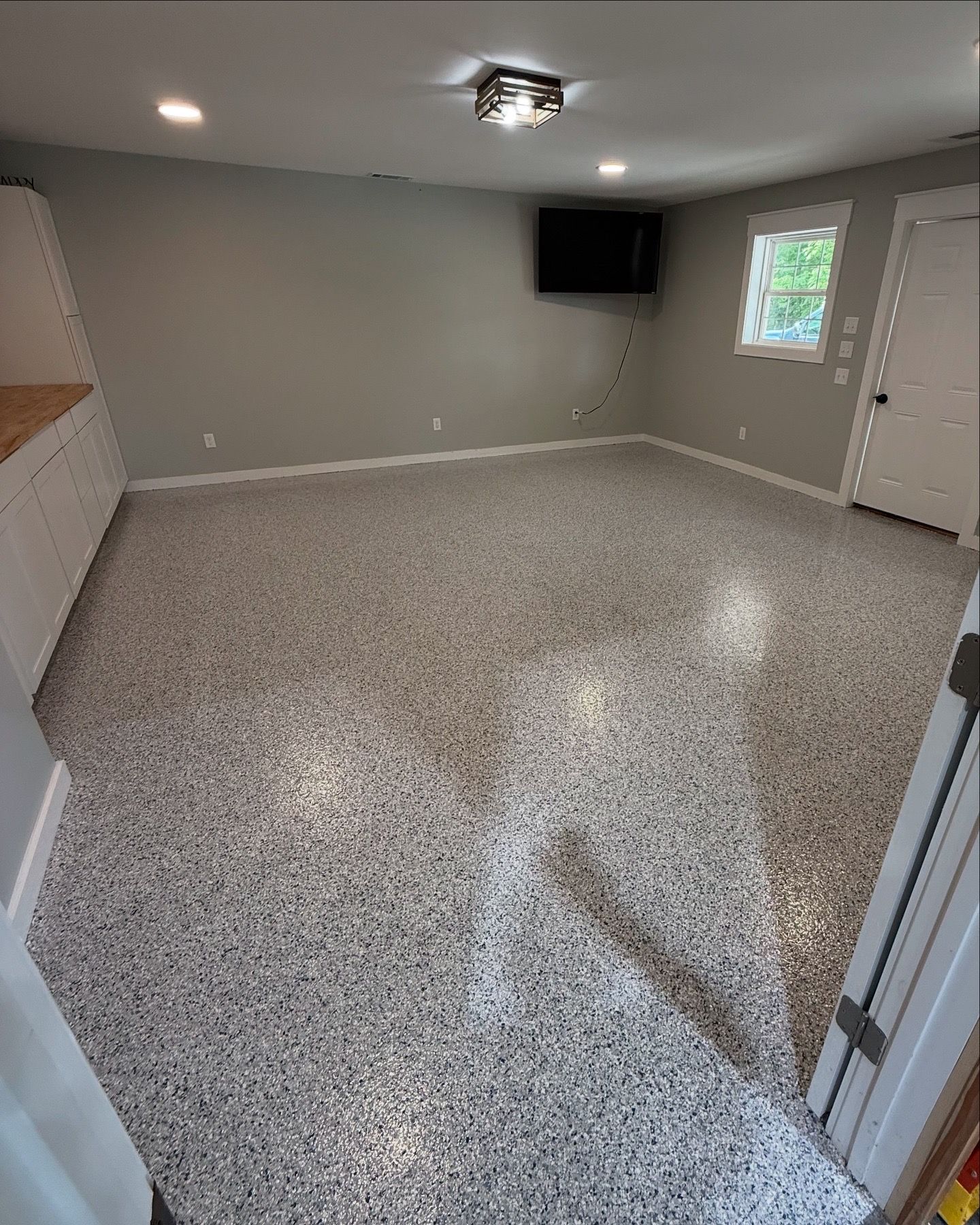 Empty room with gray speckle floor, gray walls, built-in white cabinets, a window, and a mounted TV.
