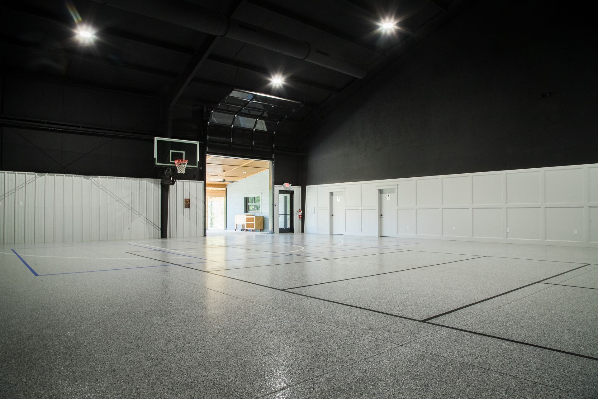 Empty indoor basketball court with black ceiling, white walls, and bright overhead lights