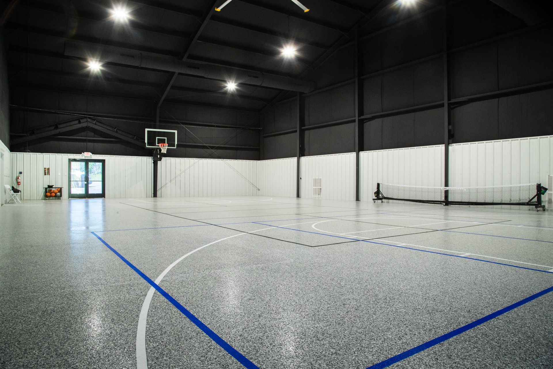 Empty indoor basketball gym with hoop, black ceiling, white walls, and blue court lines