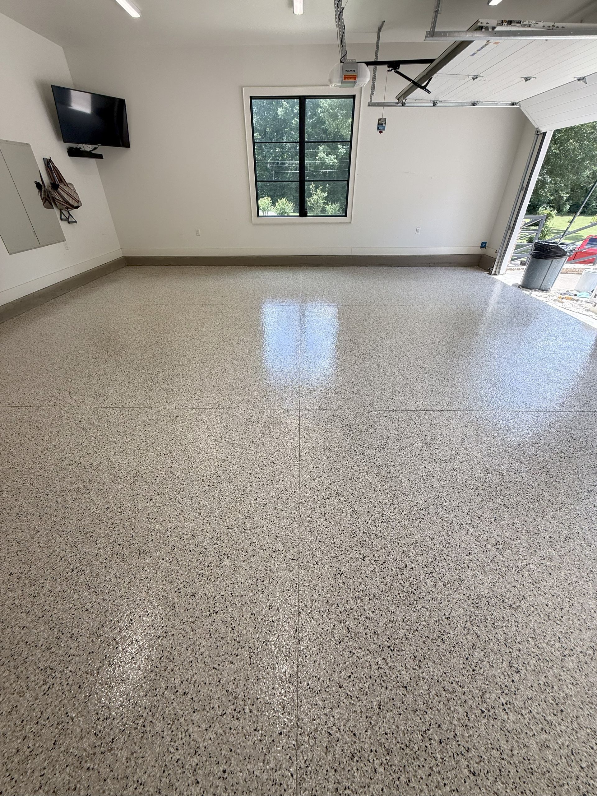Garage with epoxy floor, window, open garage door, white walls, and a television.